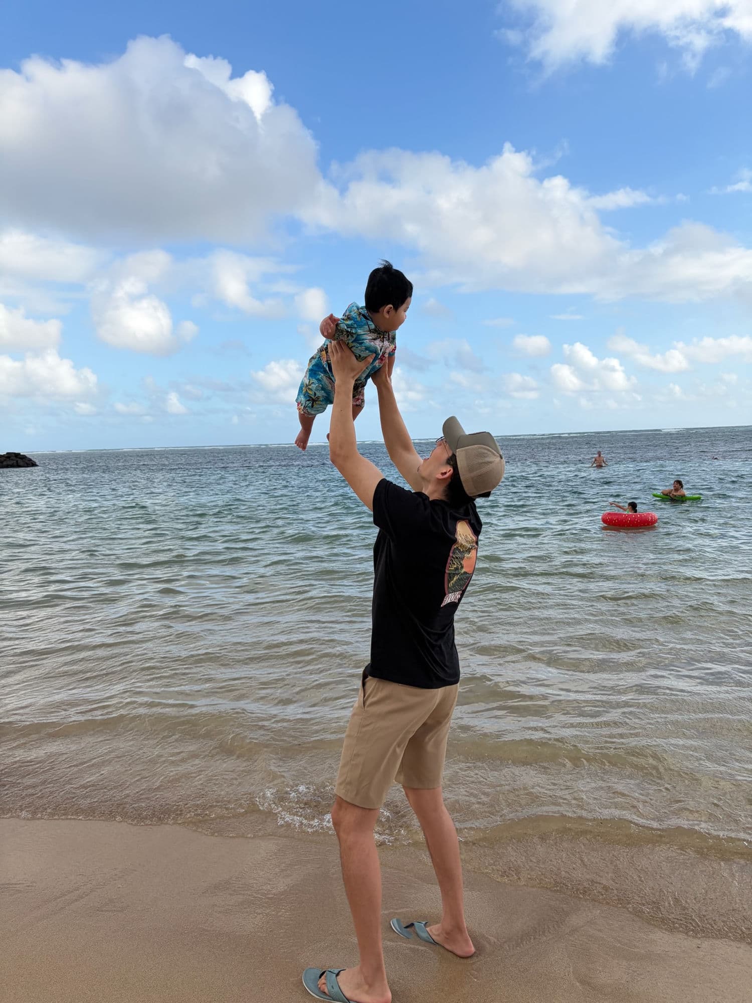 Anzhe lifting his son above the surf on a Hawaiian beach.